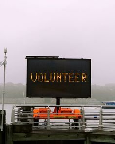 This may contain: a sign that says volunteer on the side of a pier with boats in the water behind it