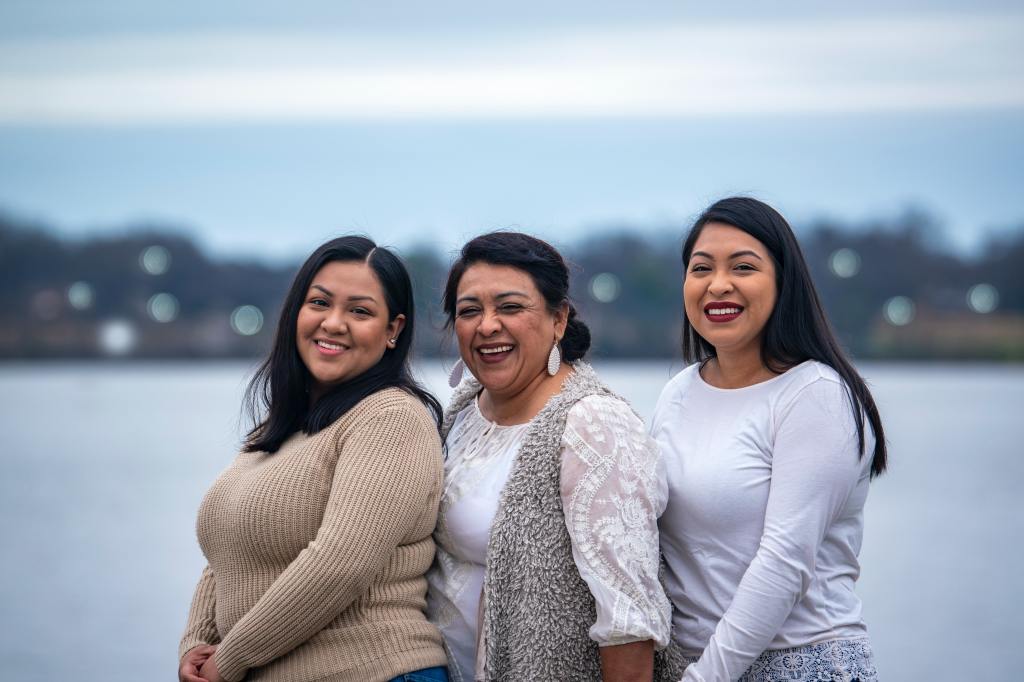 Three Latina women, a mom and her two daughters, smiling.