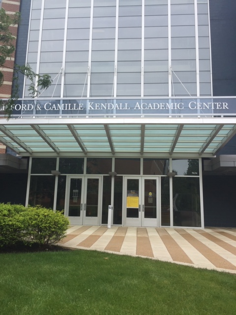 A modern looking building with lots of windows and a striped concrete entryway. Image Text: "Clifford and Camille Kendall Academic Center."