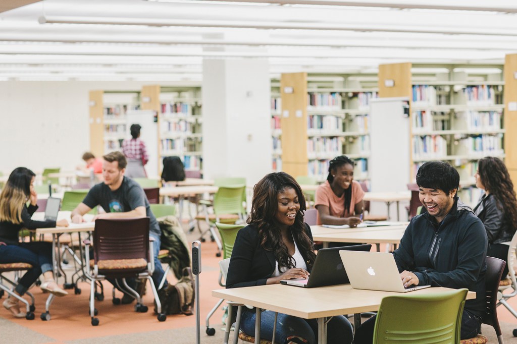 An open space full of tables, chairs, and students of all races and genders.